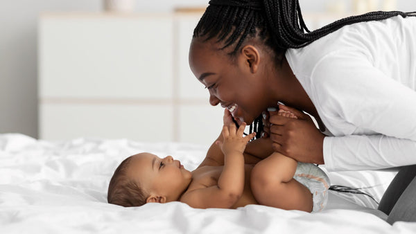 African American mother cuddling her baby on the bed. Concept of cuddling your baby having health benefits.