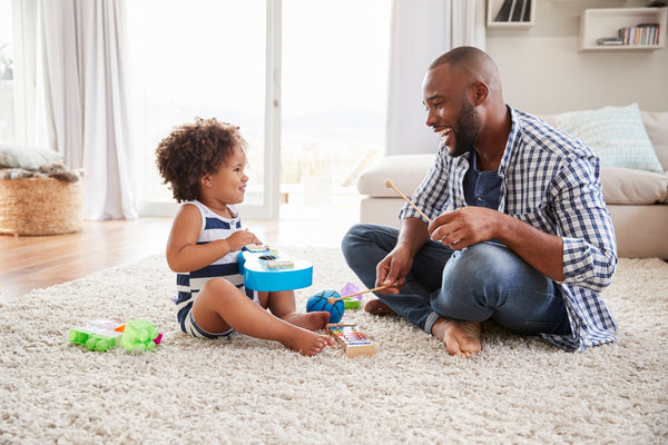 A smiling black toddler sits on the floor with her father, surrounded by toys. Concept of toddler parenting, single parent.