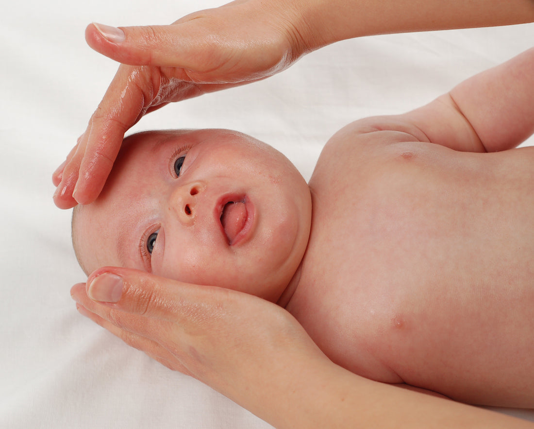 A mother applying natural oil to her baby who is lying on a bed. Concept of natural oils for baby, baby skin, baby health.