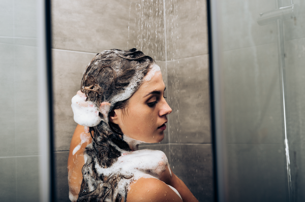 A woman using baby shampoo in the shower. Glass doors, lather, shower room. Concept of adults using baby products.