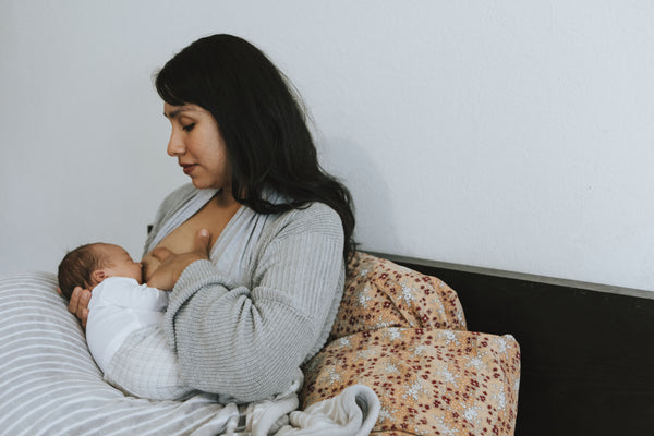 A young mother breastfeeding her baby on the bed. Concept of breastfeeding, new mother, and new baby.