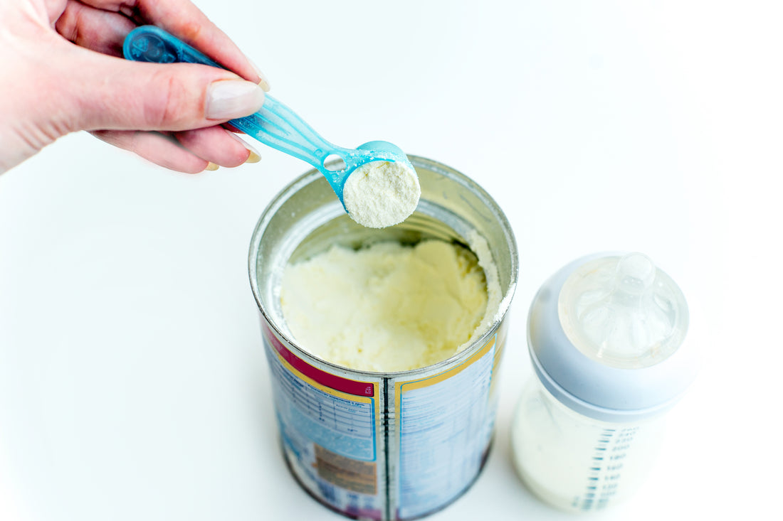 An open can of baby formula with a spoon and a baby feeding bottle nearby. 