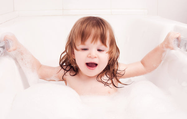 A toddler with long hair sitting in a bathtub and enjoying a bubble bath. Concept of fun bath time for kids.