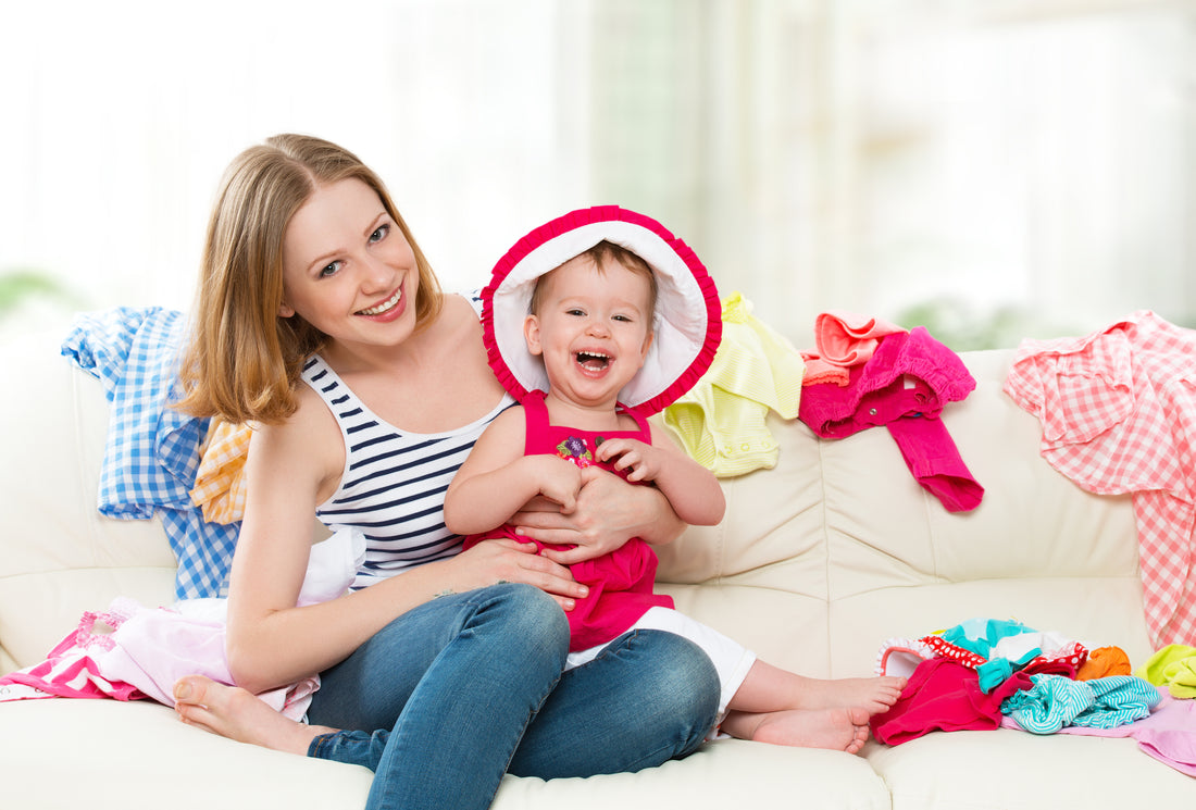 A mother and baby sitting on a sofa surrounded by the baby's outgrown clothes, ready to indulge in some repurposing and upcycling.