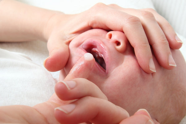 A mother holding her crying newborn's baby's face and checking the mouth for oral thrush.