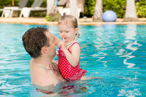 A father and his toddler daughter in a pool during a hot summer's day
