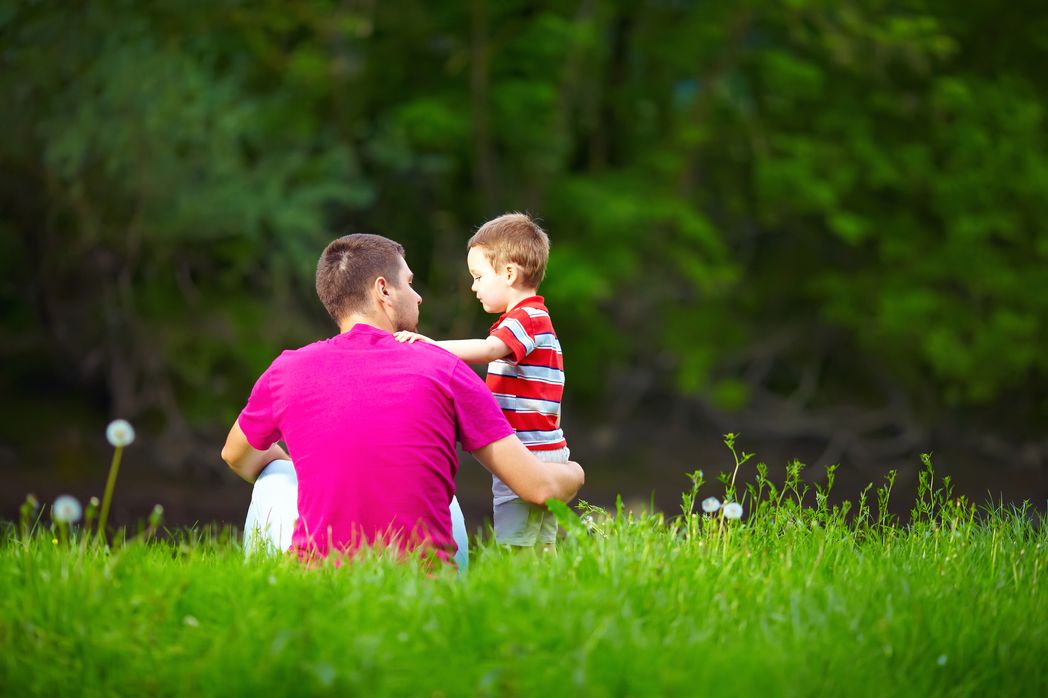 A father and his toddler in a grassy park.
